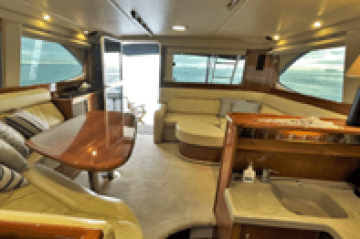 Interior of luxury yacht with wooden table, sofa, and kitchenette.