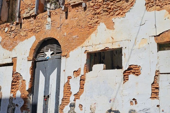 Old brick building with murals and a star-painted door, showing urban decay under a clear blue sky.